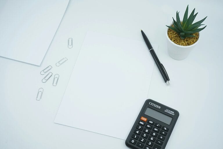 Calculator, pen, and blank paper on a desk, representing computing 14th month pay in the Philippines