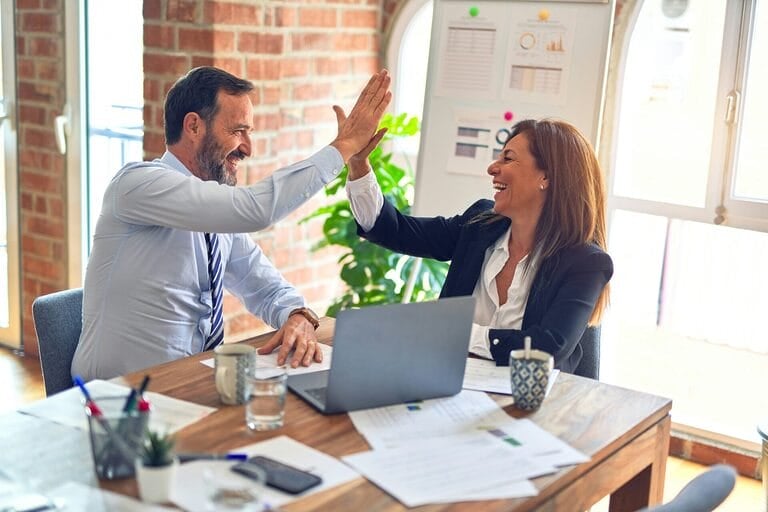 Two coworkers celebrating with a high five in the office, representing an employee becoming a regular employee in the Philippines