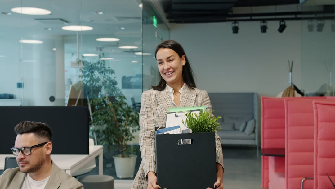 Filipino employee smiling and carrying a box of personal belongings while saying goodbye to coworkers on her last day, illustrating a voluntary resignation from a job in the Philippines