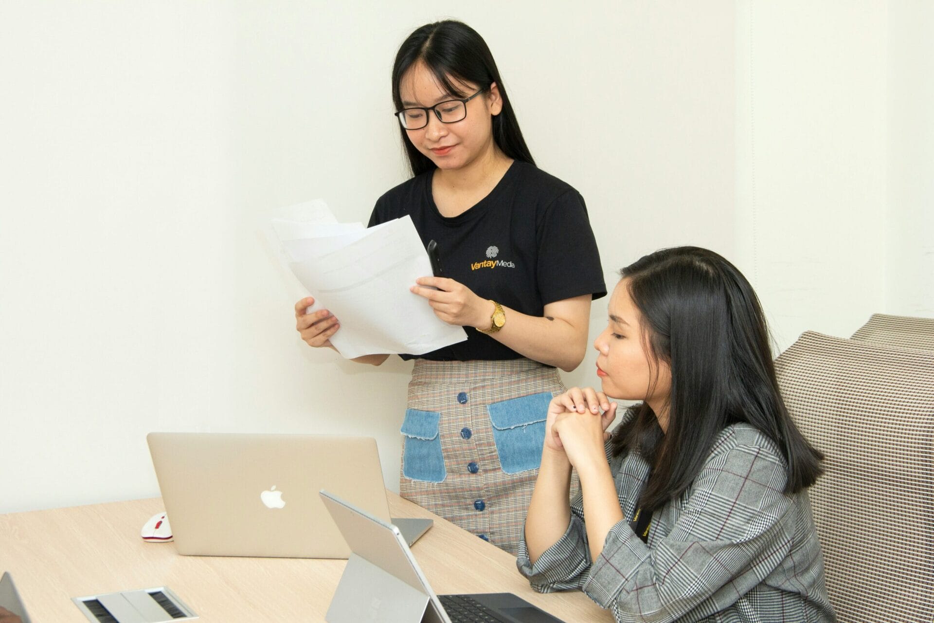 Two women work together at a desk, discussing what is separation pay in the Philippines with their laptops.