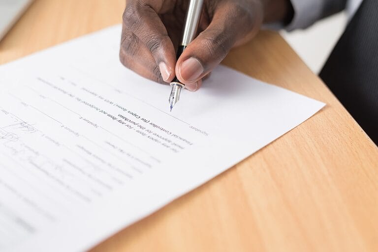 Close-up of a hand writing and signing a formal resignation letter on paper, illustrating the 30-day notice resignation letter template
