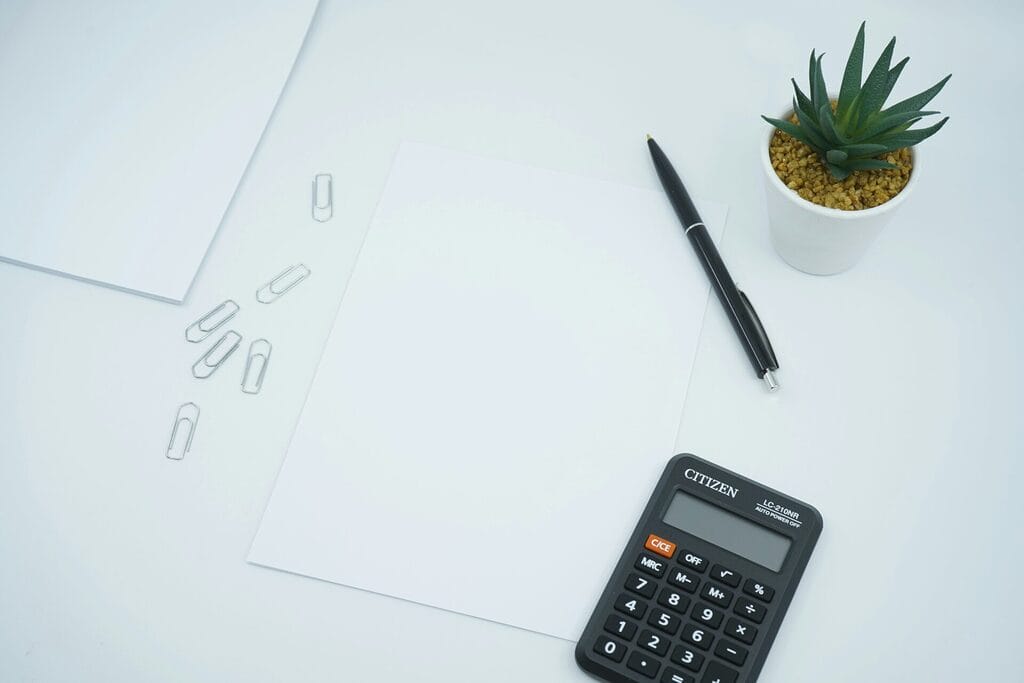 Calculator and blank worksheet on a desk used to compute an SSS monthly contribution, showing the employer and employee share calculation for a Philippine payroll