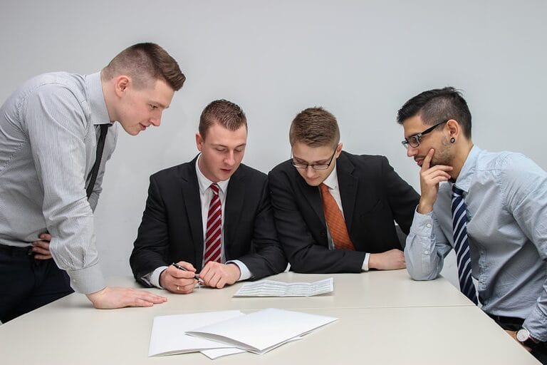 Four people at a table closely reviewing a written document together, representing employer and union negotiators going over a collective bargaining agreement proposal